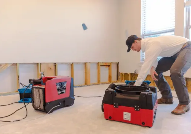 Technician setting drying equipment in a room with the lower walls flood cut