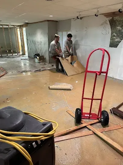 Two workers pulling up soaked flooring in a lower-level room