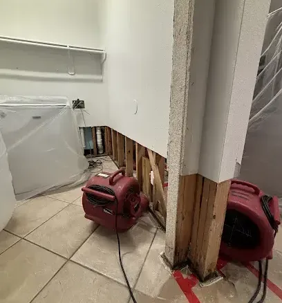 Baseboards pulled off and air movers drying the bottom of a wall