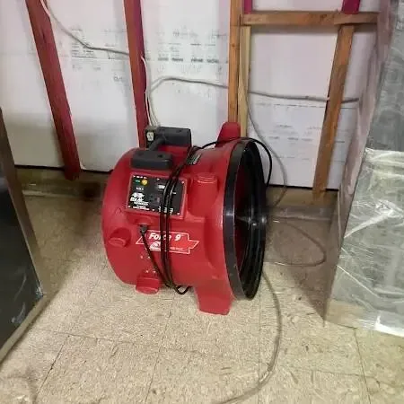 Red air mover running on a tile floor beside an opened wall