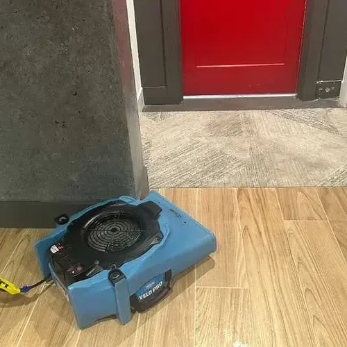Blue air mover resting on a wood look tile floor beside an open doorway