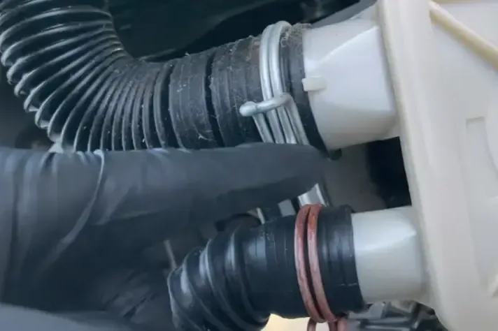 Gloved hand checking the drain hose fittings behind a washing machine